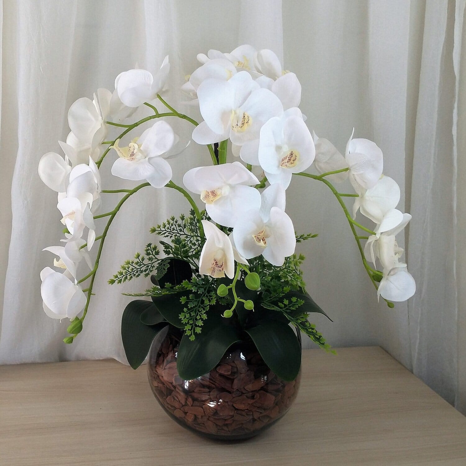 Orquídeas brancas em vaso decorativo com folhagens verdes.