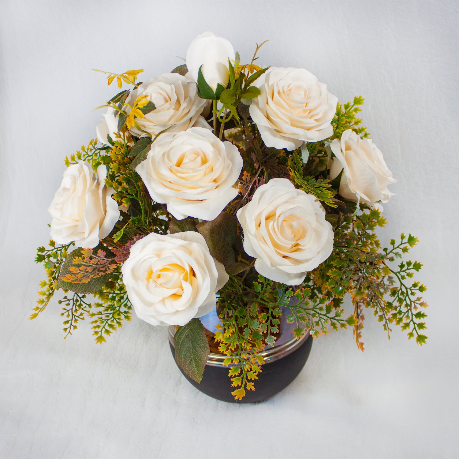 Ramo de rosas brancas em vaso decorativo branco com folhagem variada.