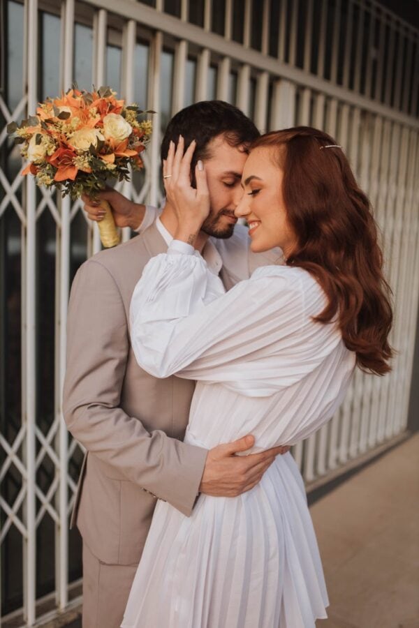 Romance entre noivos com buquê de flores, abraço e alegria no casamento.