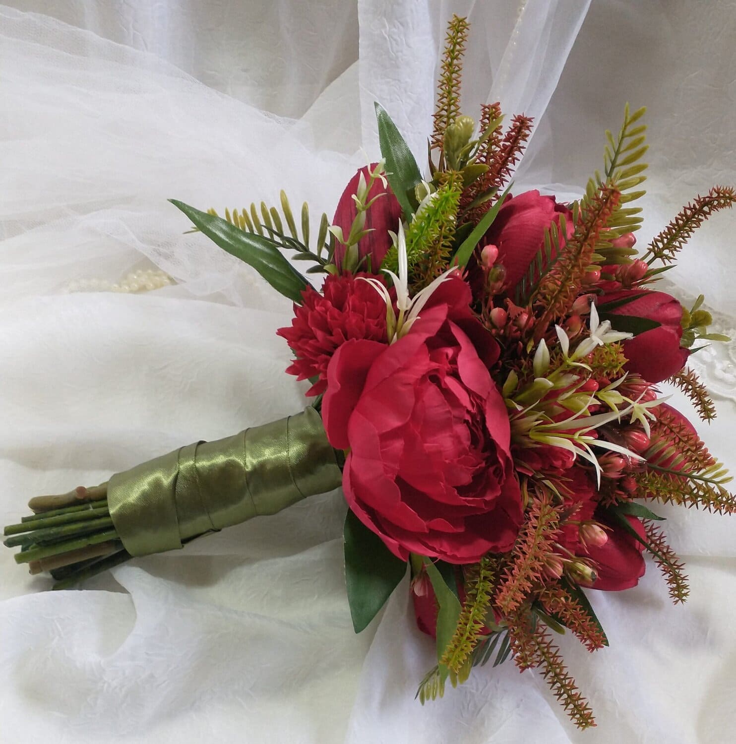 Buquê de flores em tons de vermelho com folhagens verdes e detalhes brancos.