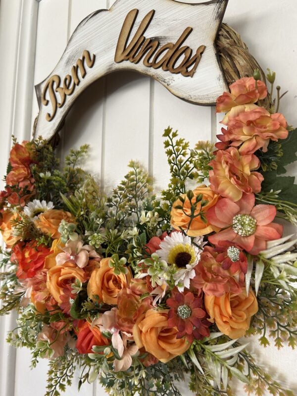 Arranjo floral decorativo com rosas e detalhes verdes, com "Bem Vindos" em madeira na moldura.