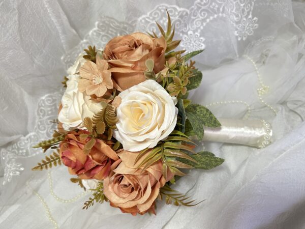 Buquê de flores bege, branco e rosado com folhagens e detalhes decorativos.