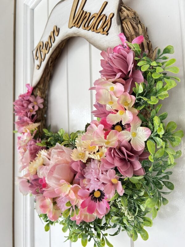 Arranjo de flores em guirlanda decorativa com rosas, cravos e folhagens em tons de rosa e verde.