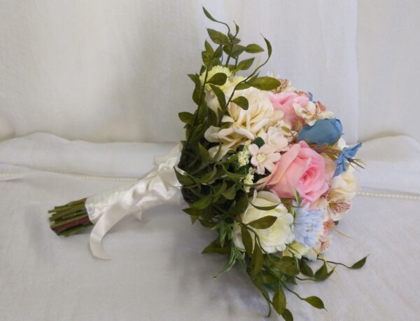 Bouquet de casamento com rosas e flores decorativas em tons pastel, com folhagem verde e fita de cetim branca.