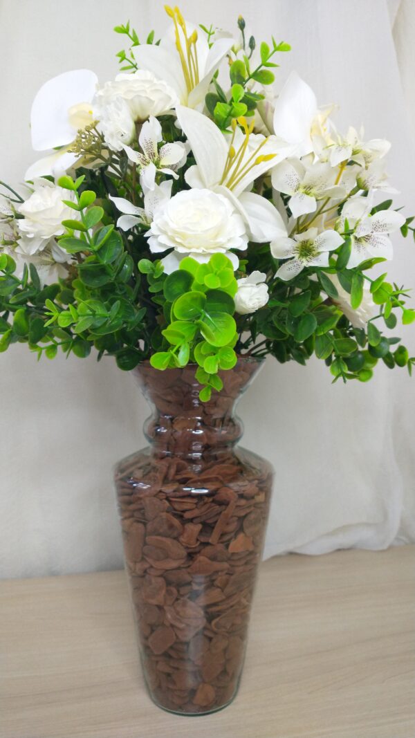 Buquê de flores brancas em vaso de vidro com pedras decorativas.