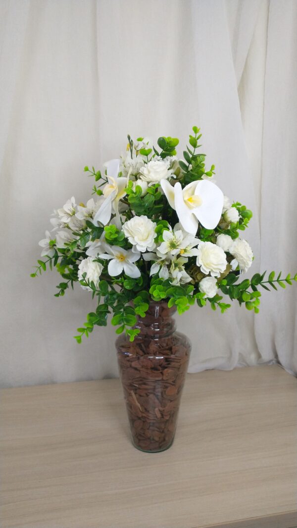 Buquê de flores brancas com orquídeas e folhagens em vaso de vidro.