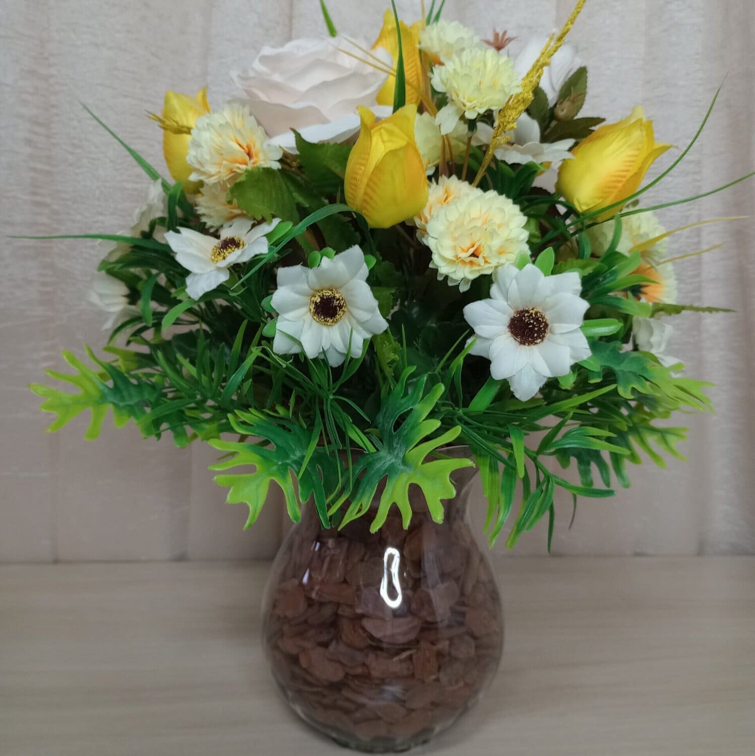 Buquê de flores com rosas amarelas, brancas e folhagem decorativa, em vaso de vidro.