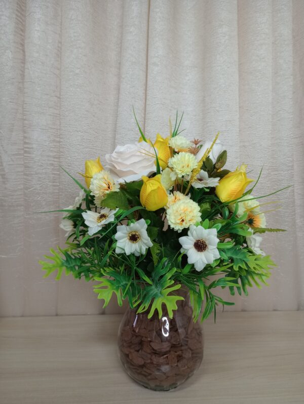 Buquê decorativo com flores artificiais em vaso de vidro com pedras.