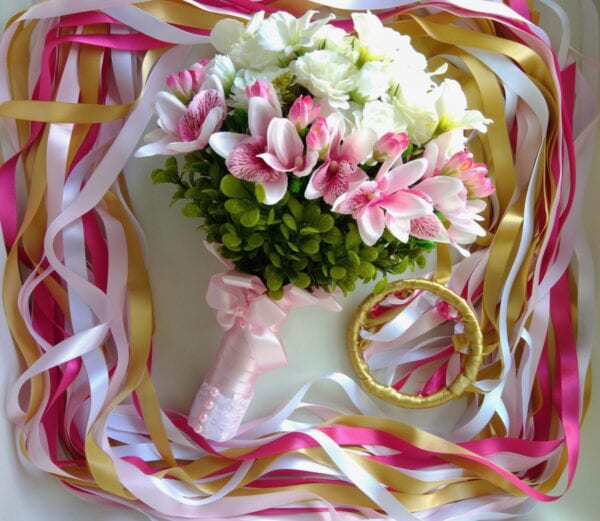 Buquê de flores com rosas e orquídeas em tons de rosa e branco, decorado com fitas coloridas.